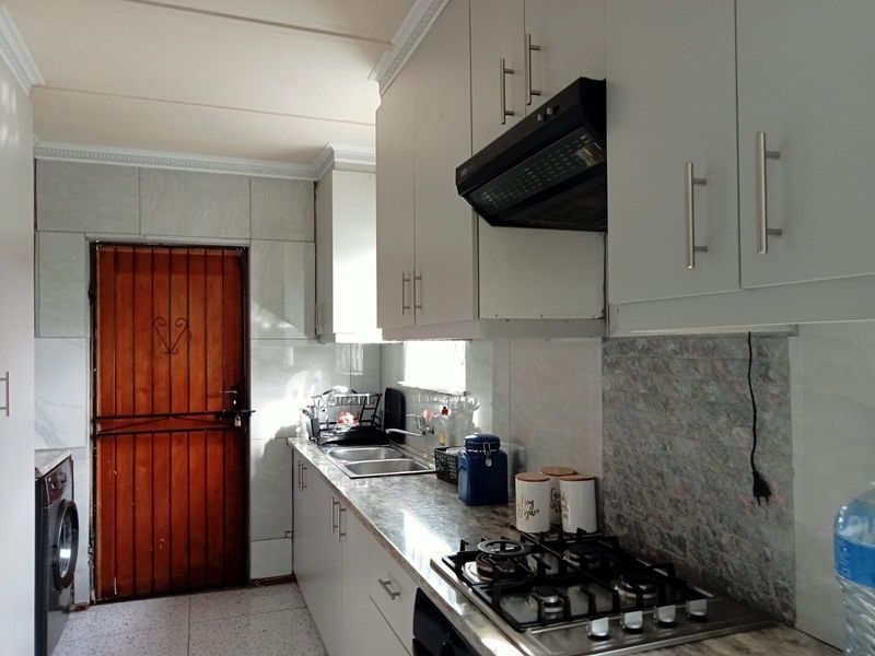 A functional kitchen featuring white built-in cabinetry, a gas hob with extractor fan, double sink, and tiled finishes with a secure rear access door.