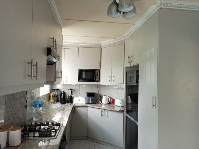 A functional kitchen featuring light-toned cabinetry, stone-look countertops, a gas hob, and a built-in microwave with a tiled backsplash.