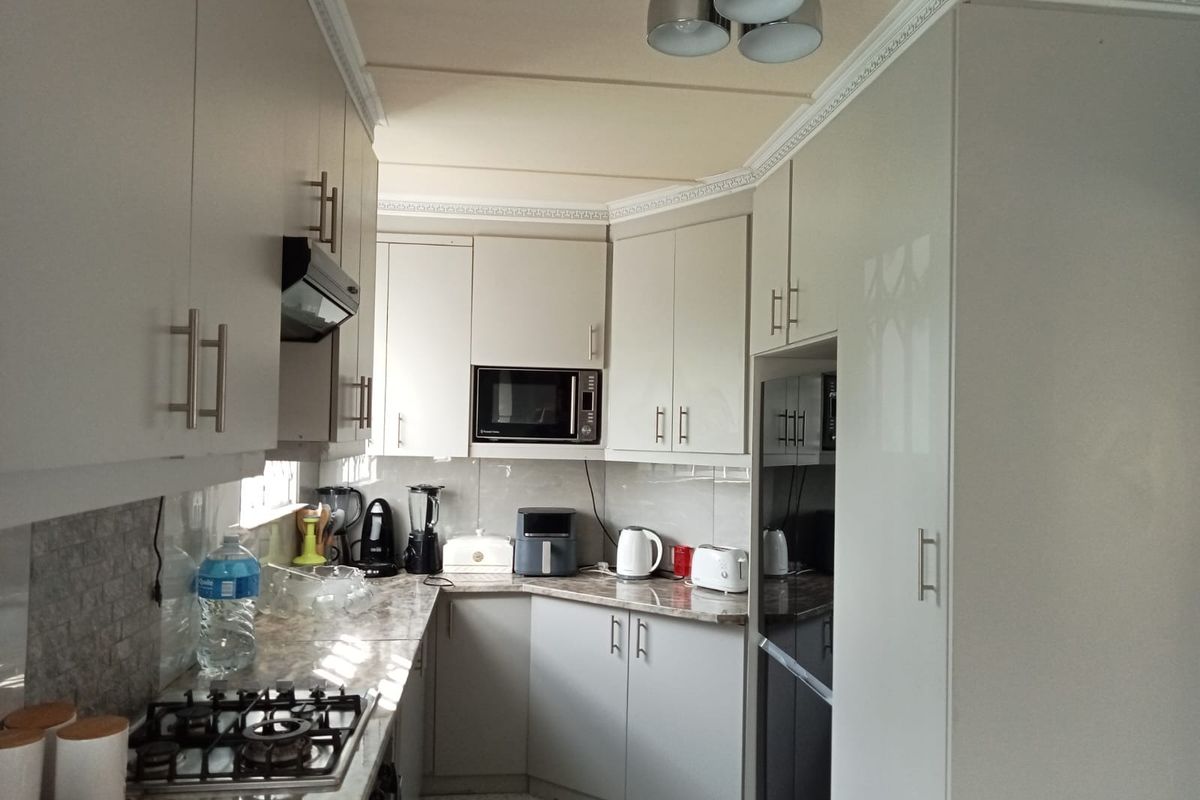 A functional kitchen featuring light-toned cabinetry, stone-look countertops, a gas hob, and a built-in microwave with a tiled backsplash.