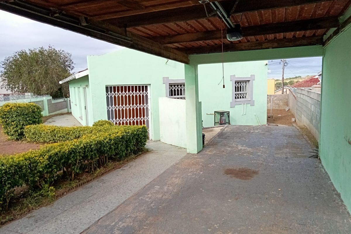 Rear exterior view featuring a covered carport, concrete driveway, and security-fitted windows and doors, set against a boundary wall and garden area.