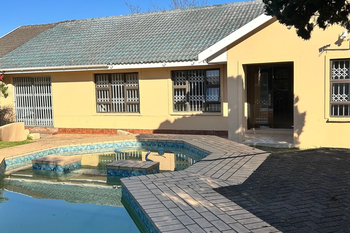Rear exterior view of the house featuring a swimming pool with tiled surround, security gates on windows, and a tiled roof.
