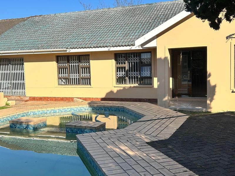 Rear exterior view of the house featuring a swimming pool with tiled surround, security gates on windows, and a tiled roof.