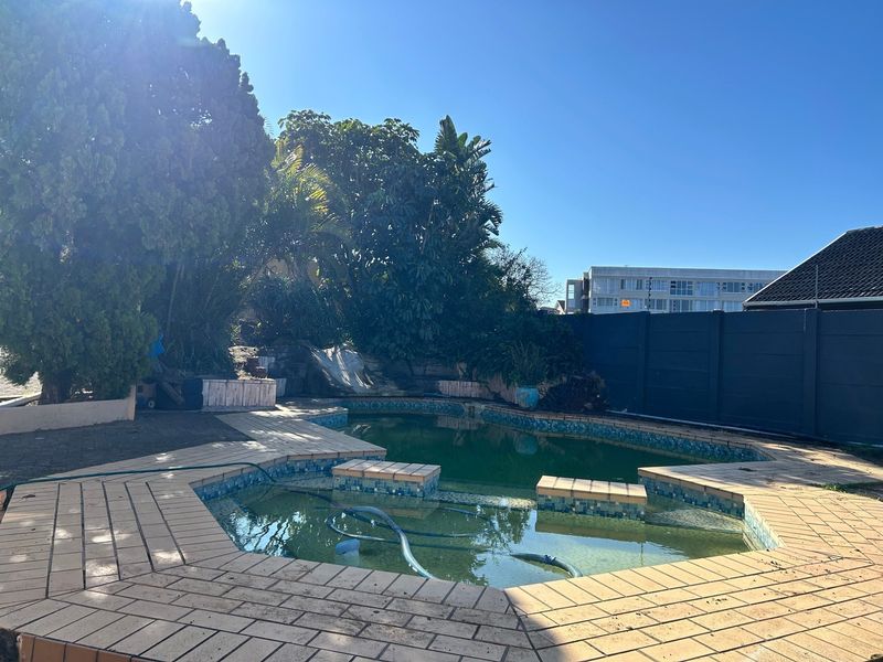 Outdoor pool area featuring a tiled surround, built-in rock feature, and boundary wall, currently requiring maintenance and pool water treatment.