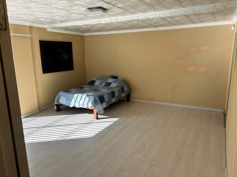 A bedroom featuring light-toned laminate flooring and a textured ceiling, requiring cosmetic updates to improve the overall finish and aesthetic appeal.