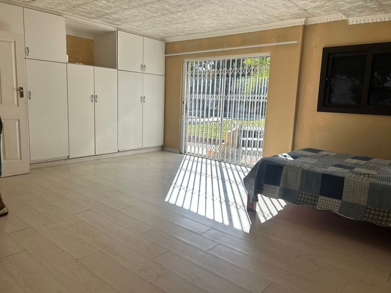 Spacious bedroom featuring built-in cupboards, light-toned tiled flooring, and a sliding glass door with a security gate providing access to the exterior.