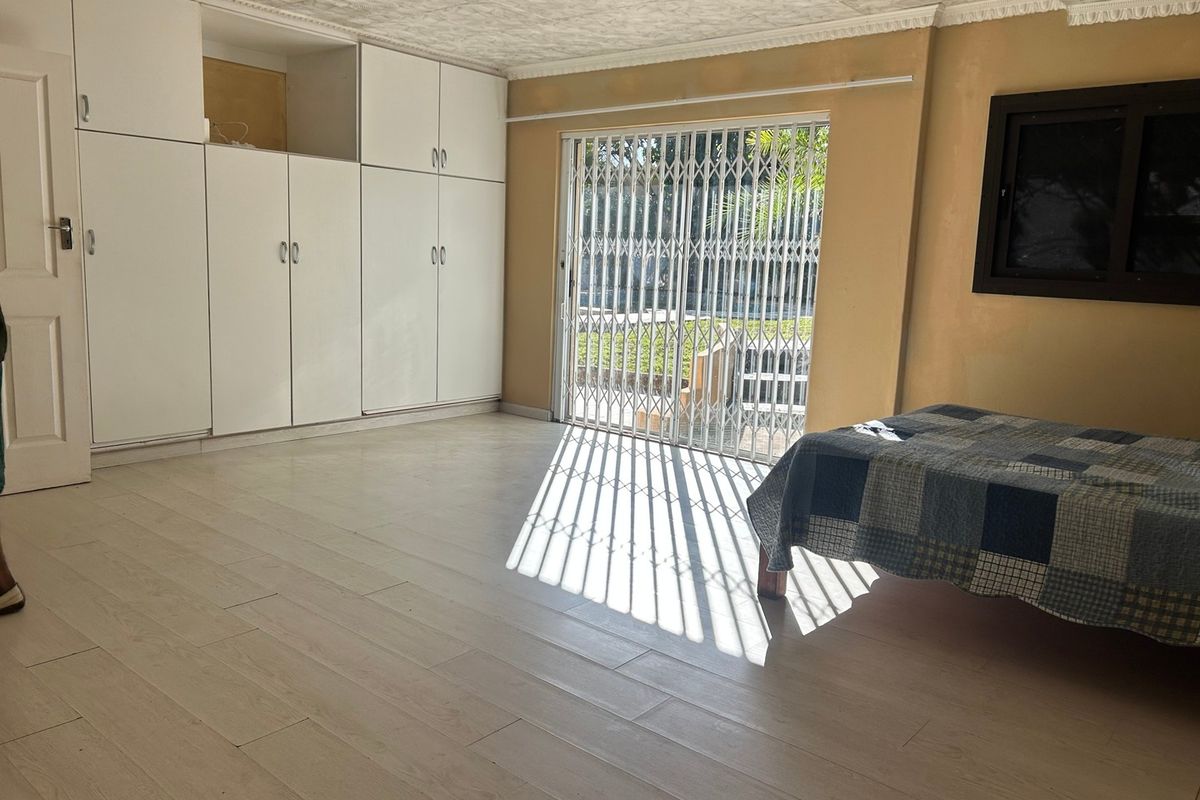 Spacious bedroom featuring built-in cupboards, light-toned tiled flooring, and a sliding glass door with a security gate providing access to the exterior.