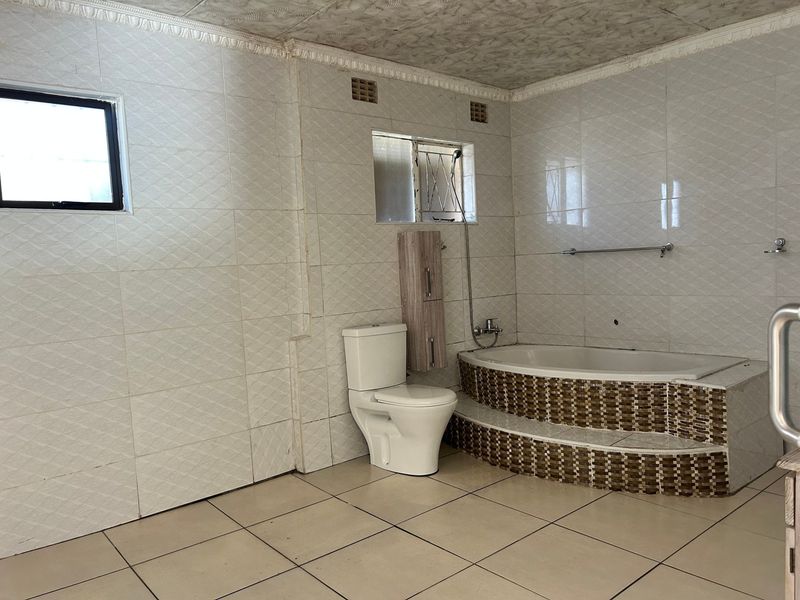 A spacious, empty bathroom featuring a built-in bathtub with a tiled surround, a toilet, and full-height wall tiling.