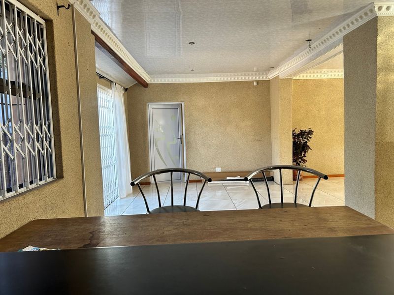 An open-plan living area featuring tiled flooring, decorative ceiling cornices, recessed lighting, and secure access points with security gates.