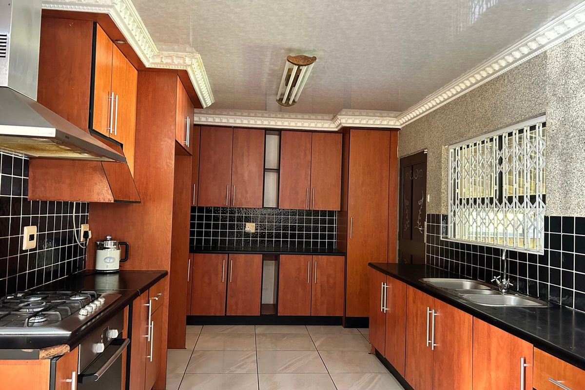 A functional kitchen featuring warm-toned wooden cabinetry, black granite countertops, a gas hob, and a double basin sink with tiled finishes.
