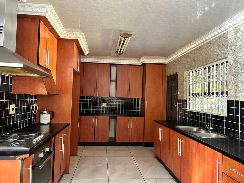 A functional kitchen featuring warm-toned wooden cabinetry, black granite countertops, a gas hob, and a double basin sink with tiled finishes.