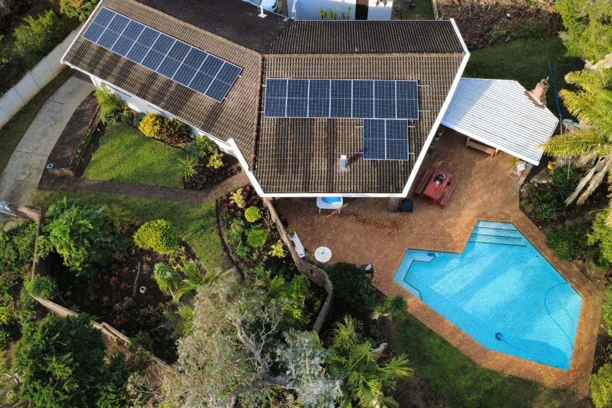 Aerial view of a residential property featuring a tiled roof with solar panels, a swimming pool, paved patio area, and established garden.