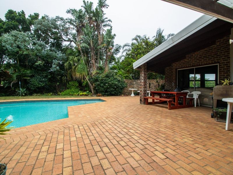 A spacious outdoor entertainment area featuring a swimming pool and a covered brick-paved patio with direct access to the home through sliding glass doors.