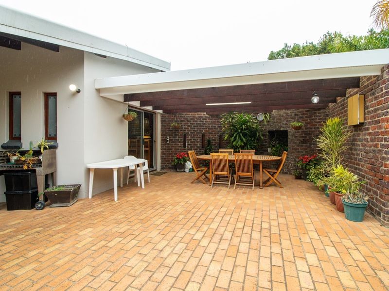 A covered outdoor patio area featuring brick paving, exposed brick walls, and a timber pergola, providing a functional space for outdoor dining and entertainment.