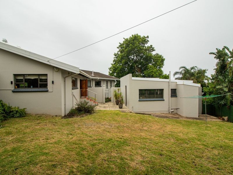 Rear view of the property featuring a paved patio area, lawn, and exterior building facade with security features.
