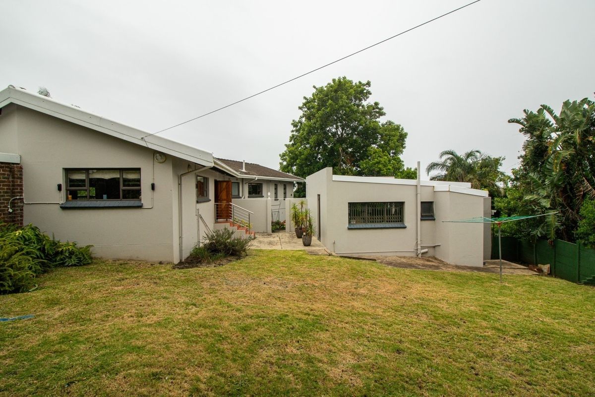 Rear view of the property featuring a paved patio area, lawn, and exterior building facade with security features.
