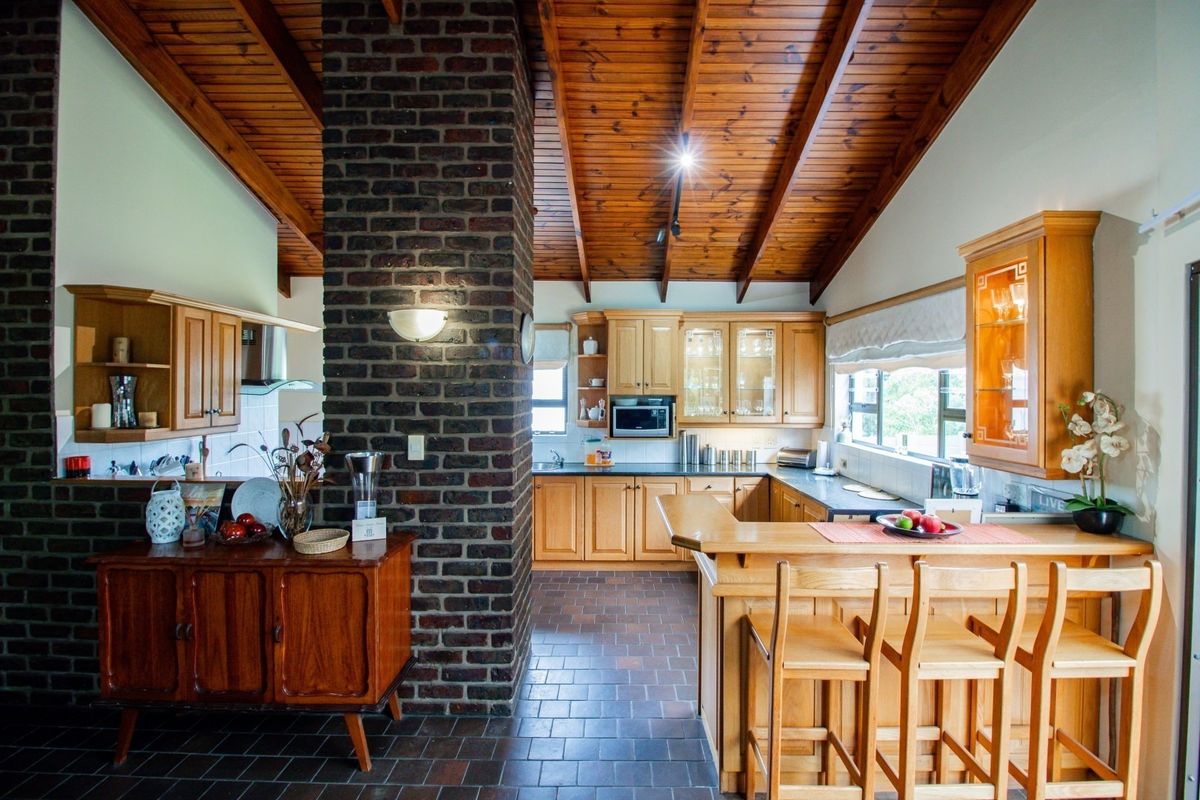 Spacious kitchen featuring a central exposed brick chimney, timber raked ceilings, wooden cabinetry, and a functional breakfast bar with tiled flooring.