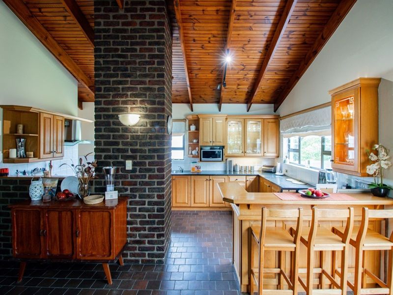Spacious kitchen featuring a central exposed brick chimney, timber raked ceilings, wooden cabinetry, and a functional breakfast bar with tiled flooring.