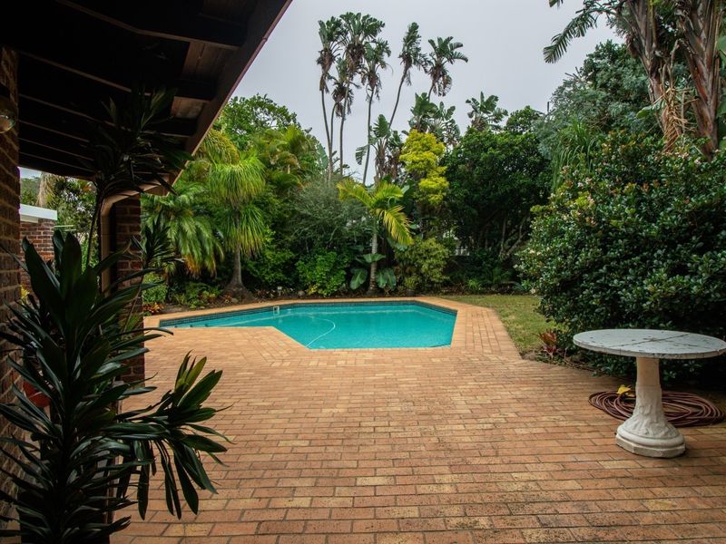 A private outdoor pool area featuring a brick-paved patio, established garden landscaping, and a covered veranda space.