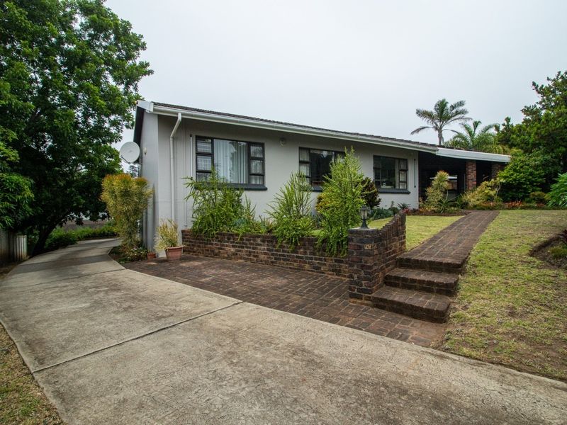 Front elevation of a single-story house featuring a concrete driveway, brick retaining wall, and landscaped garden with paved walkway access.