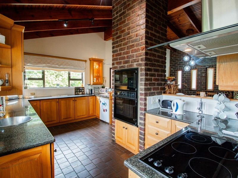 Spacious kitchen featuring exposed timber beams, a brick feature wall, granite countertops, and ample wooden cabinetry with integrated appliances.