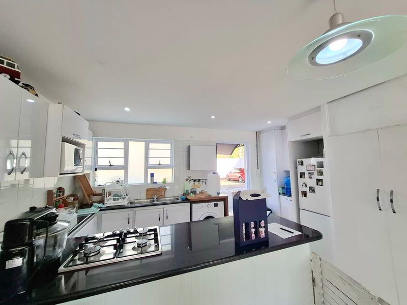 Functional kitchen featuring a gas hob, granite countertops, double sink, and built-in cabinetry with integrated laundry space and direct exterior access.