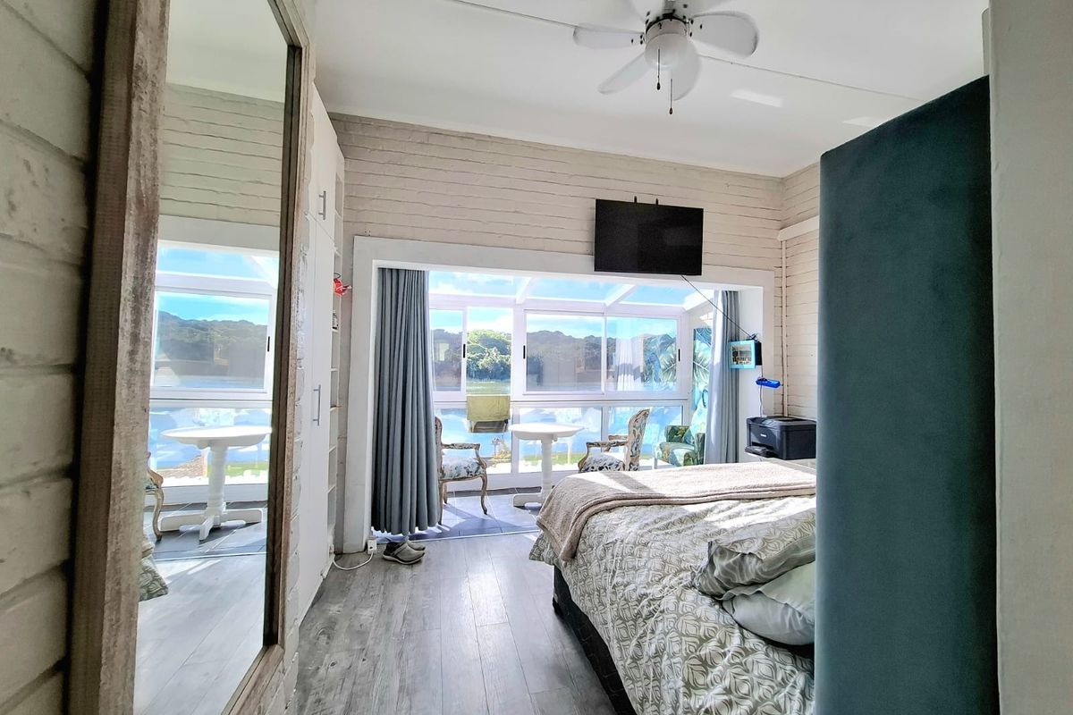 A bright bedroom featuring painted brick walls, laminate flooring, a ceiling fan, and large sliding glass doors opening to an outdoor patio area.