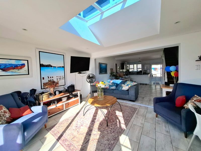 Spacious open-plan living area featuring a large skylight, tiled flooring, and recessed lighting, seamlessly connecting to the kitchen space.