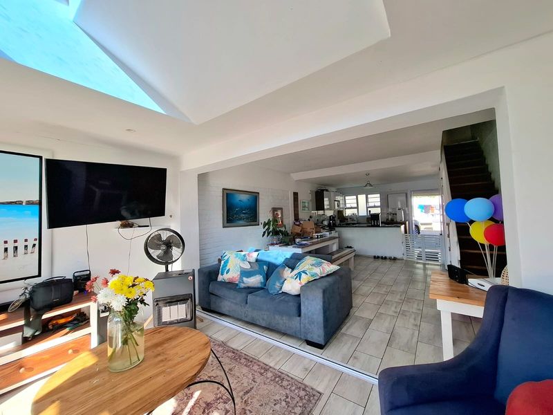 Spacious open-plan living and kitchen area featuring a large skylight, tiled flooring, and an exposed brick wall, creating a bright and airy atmosphere.
