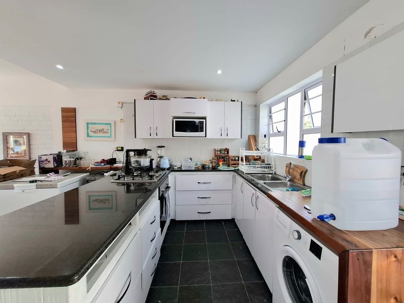 Functional kitchen featuring white cabinetry, granite countertops, built-in appliances, and tiled flooring, offering a practical layout for daily cooking and laundry needs.