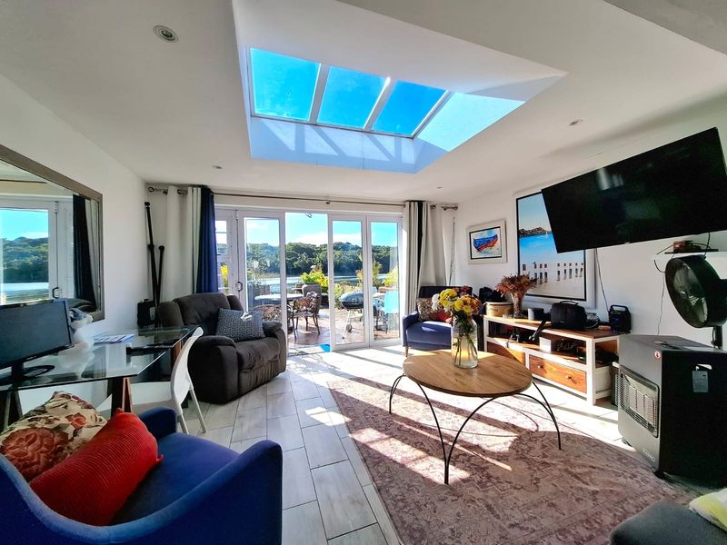 Bright living room featuring a large skylight, tiled flooring, and sliding glass doors that open onto an outdoor patio area.