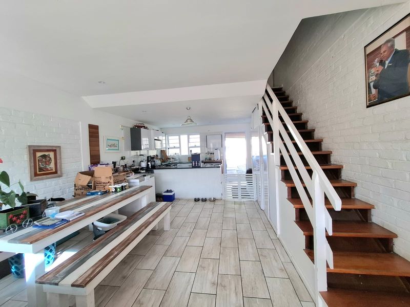 Open-plan living and kitchen area featuring a staircase with wooden treads, painted brick walls, and modern tiled flooring throughout the ground level.