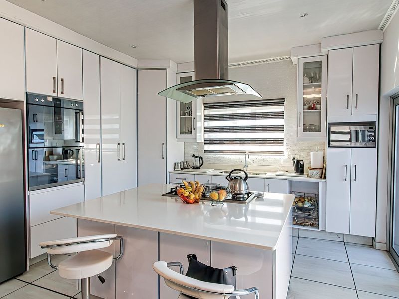 Modern kitchen featuring white cabinetry, a central island with a cooktop, built-in appliances, and large glass sliding doors providing natural light.