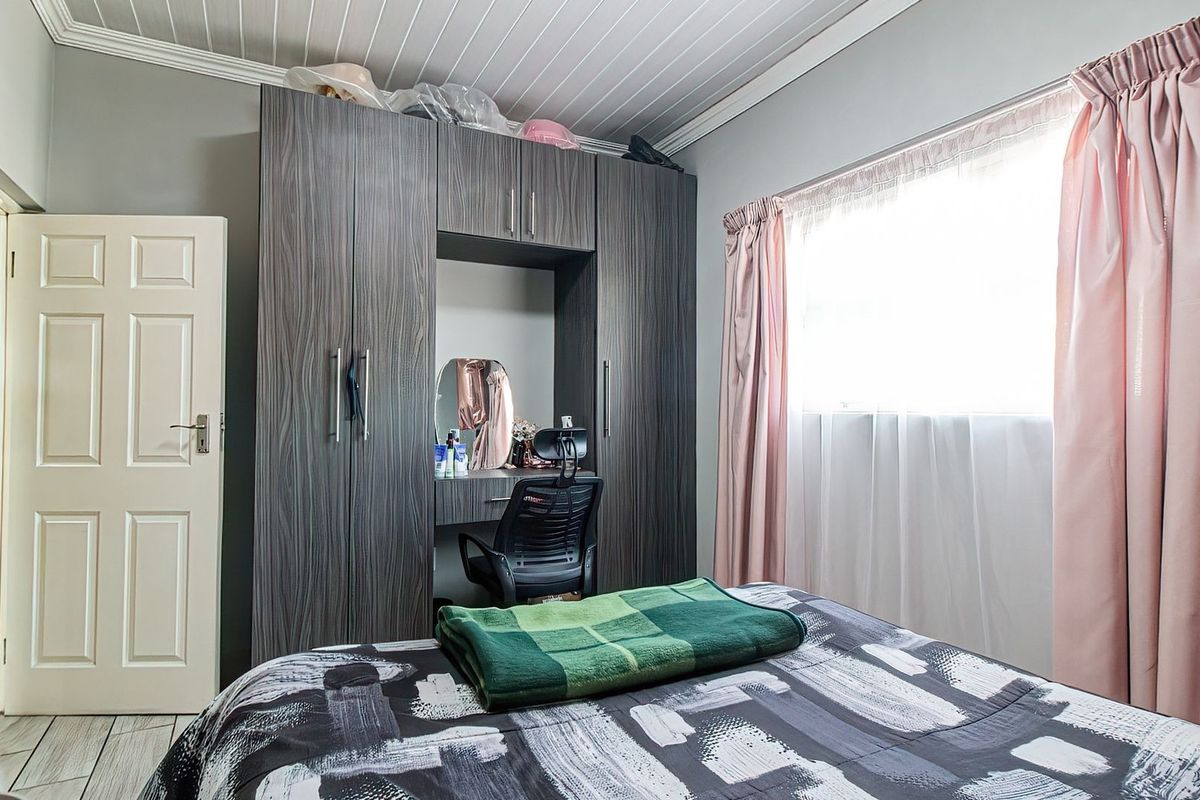 A well-maintained bedroom featuring a large built-in wardrobe with integrated vanity, tongue and groove ceiling, and tiled flooring.