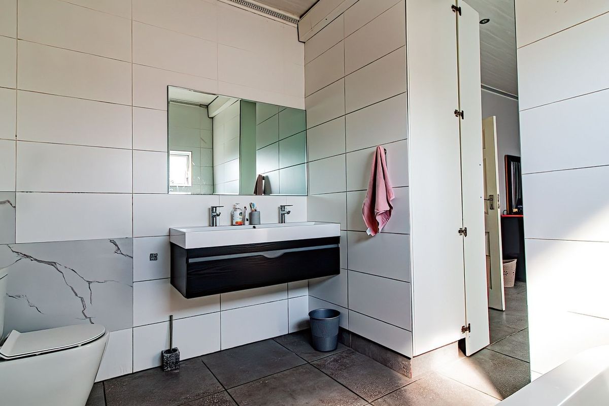 Modern bathroom featuring a wall-mounted dual vanity, large mirror, contemporary wall and floor tiling, and a sleek toilet.