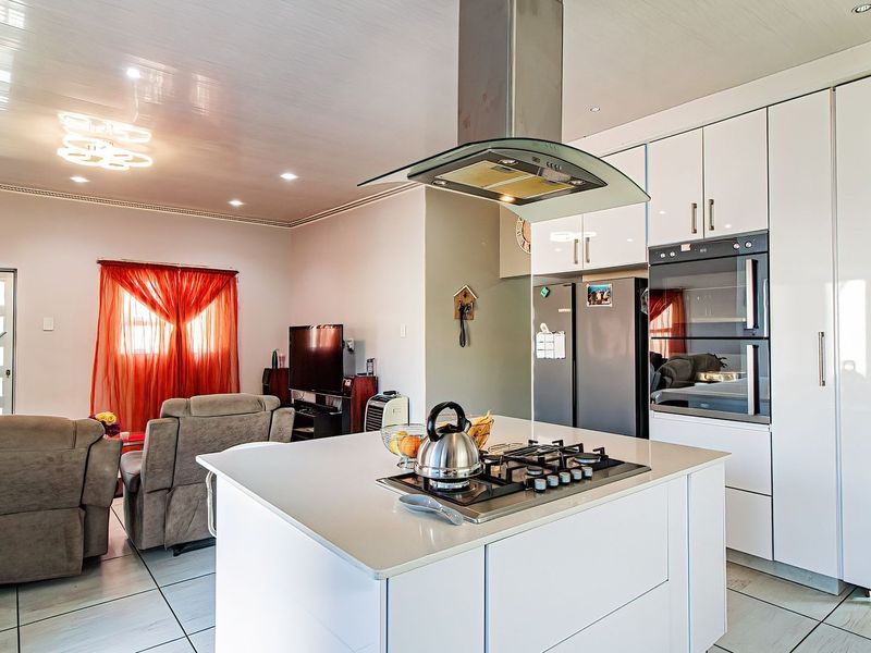 Modern open-plan living area featuring a sleek kitchen with a central island, gas hob, extractor fan, and integrated cabinetry, flowing into the lounge space.