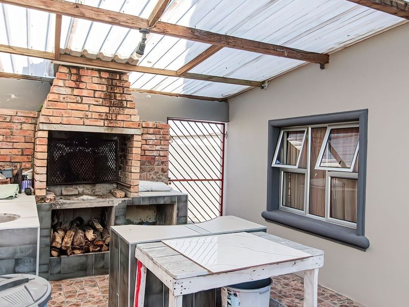 Covered outdoor patio featuring a built-in brick braai, tiled prep area with sink, and secure access, ideal for outdoor entertaining.