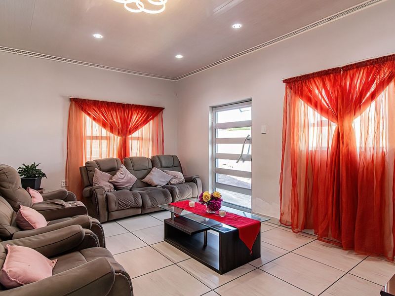 A bright and spacious living room featuring neutral tiled flooring, recessed lighting, and a modern glass-panelled entrance door.