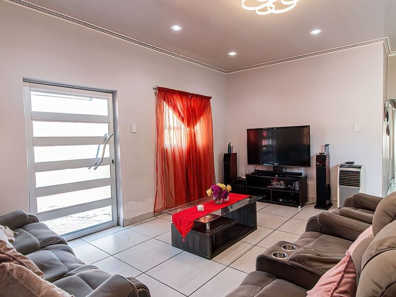 A well-lit living room featuring tiled flooring, recessed downlighting, and a glass-panelled exterior door, providing a functional and comfortable living space.