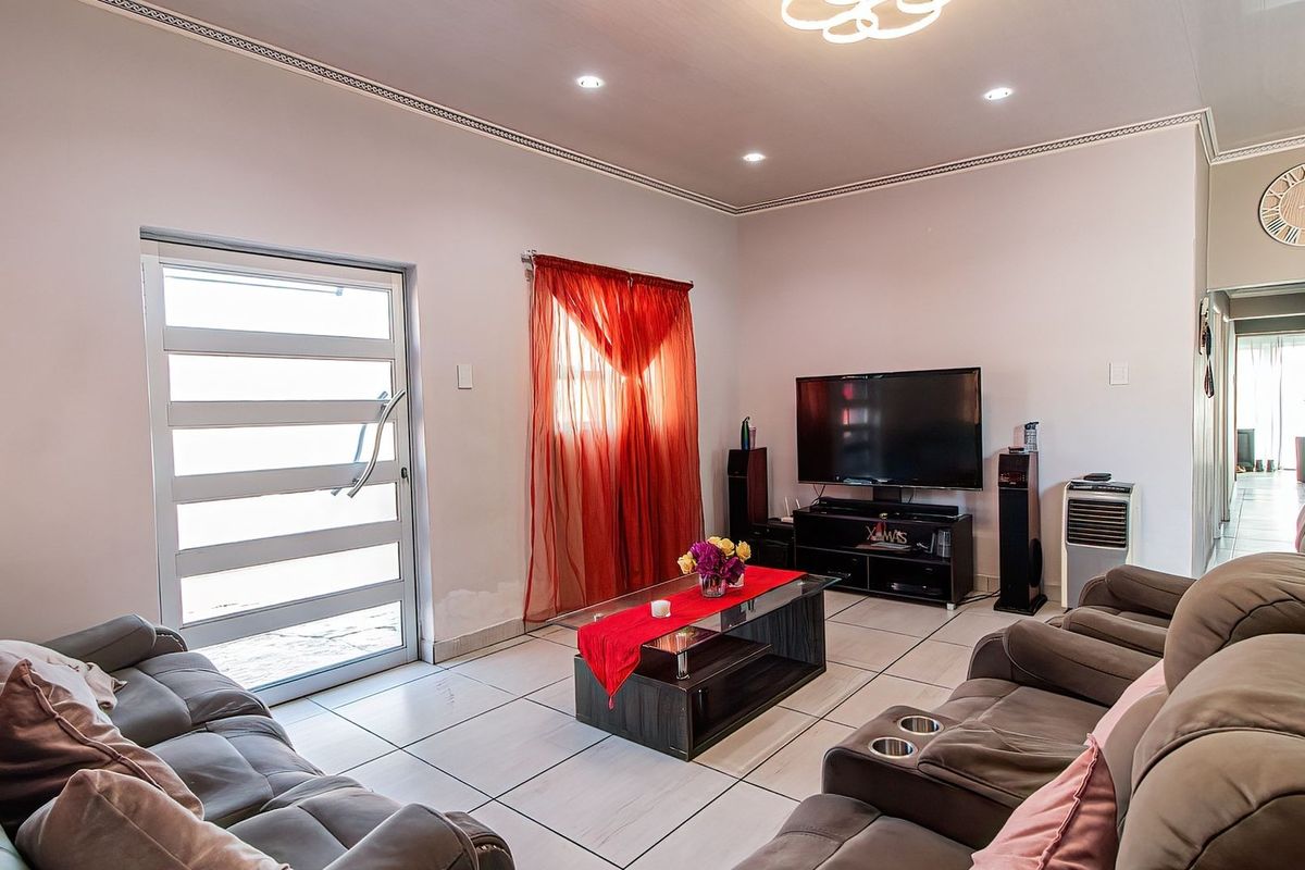 A well-lit living room featuring tiled flooring, recessed downlighting, and a glass-panelled exterior door, providing a functional and comfortable living space.