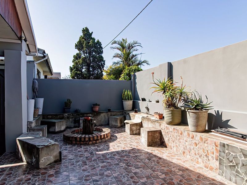 Outdoor patio area featuring a built-in brick fire pit, concrete seating, and tiled flooring, enclosed by a high perimeter boundary wall.