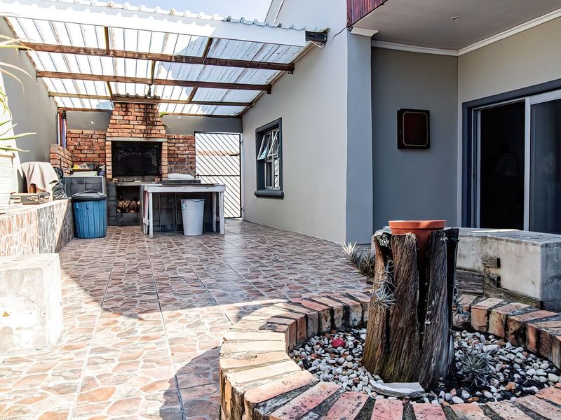 Covered outdoor patio area featuring a built-in brick braai, tiled flooring, and a decorative brick-edged garden feature, providing a functional space for outdoor entertaining.