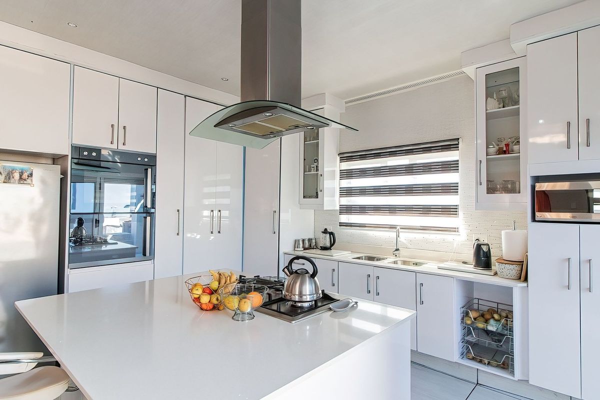 Modern kitchen featuring white cabinetry, a central island with a built-in cooktop, quartz countertops, and integrated appliances.