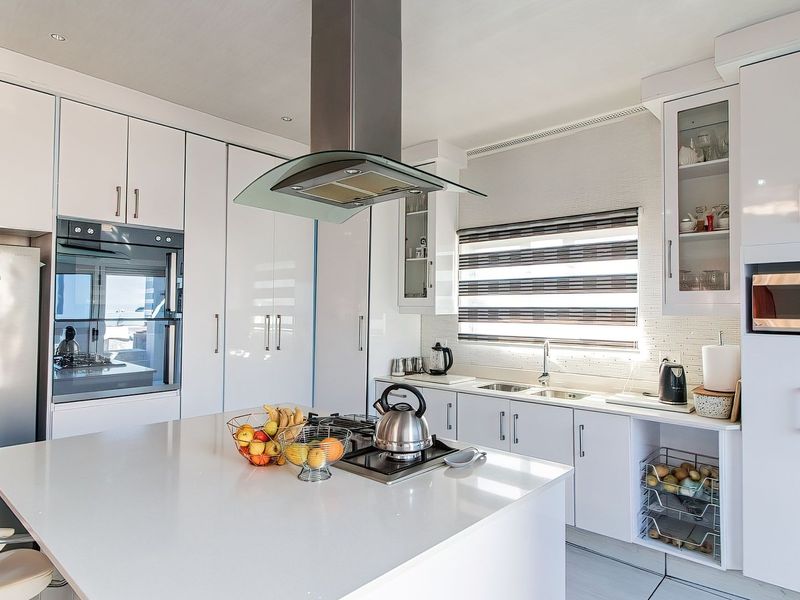 Modern kitchen featuring white cabinetry, a central island with a built-in cooktop, quartz countertops, and integrated appliances.