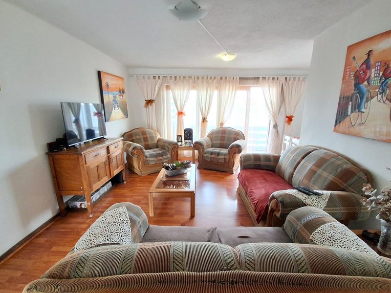 A comfortable living room featuring warm-toned laminate flooring and a large sliding glass door that provides natural light and access to the outdoors.