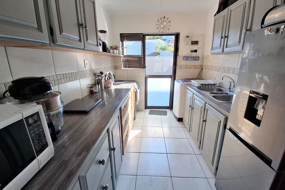 A functional galley-style kitchen featuring grey cabinetry, laminate countertops, tiled flooring, and direct access to an outdoor area.