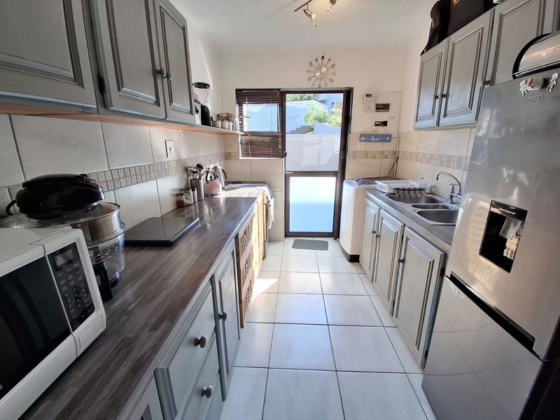 A functional galley-style kitchen featuring grey cabinetry, laminate countertops, tiled flooring, and direct access to an outdoor area.