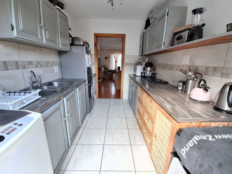 A functional galley-style kitchen featuring tiled flooring, a double basin sink, laminate countertops, and ample built-in cabinetry with a neutral backsplash.