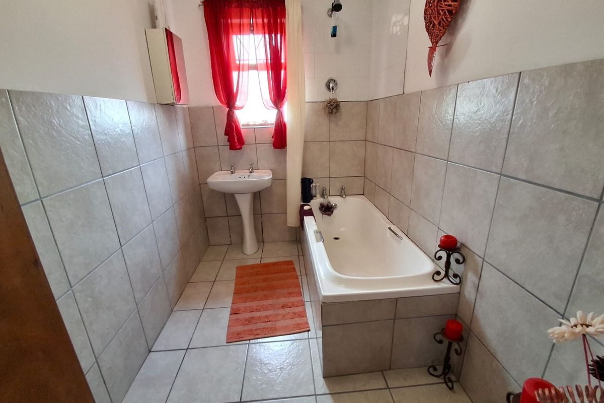 A functional bathroom featuring a pedestal basin, a built-in bathtub with shower attachment, and neutral ceramic tiling throughout.
