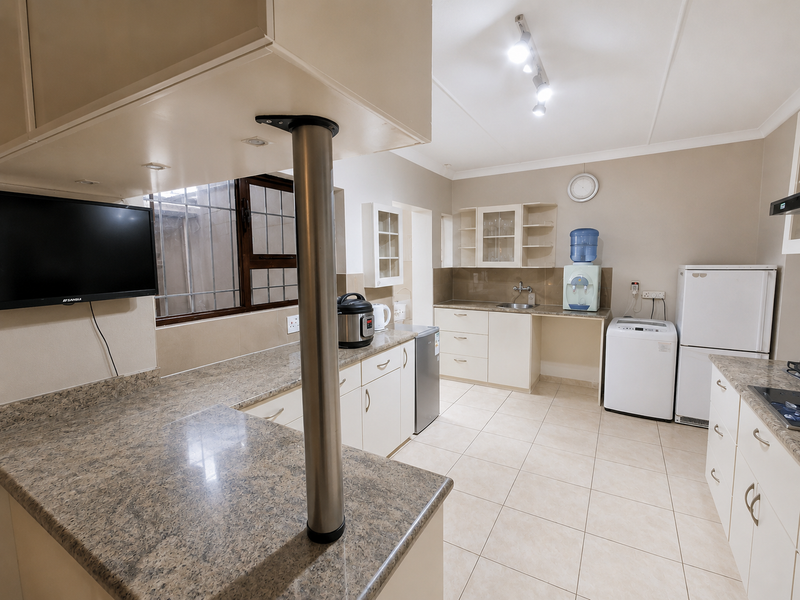 A functional kitchen featuring granite countertops, ample built-in cabinetry, ceramic tile flooring, and a central breakfast bar with a stainless steel support column.