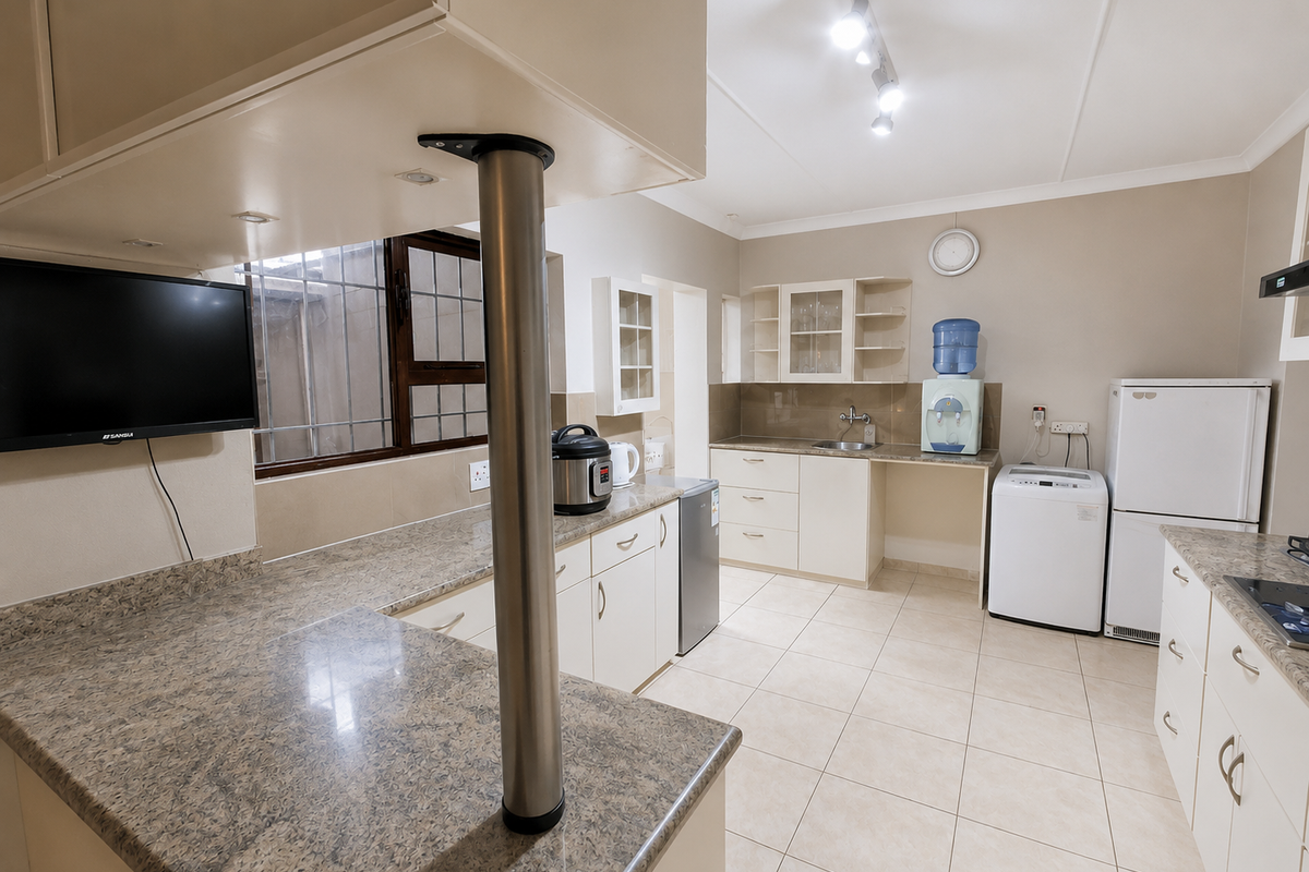 A functional kitchen featuring granite countertops, ample built-in cabinetry, ceramic tile flooring, and a central breakfast bar with a stainless steel support column.